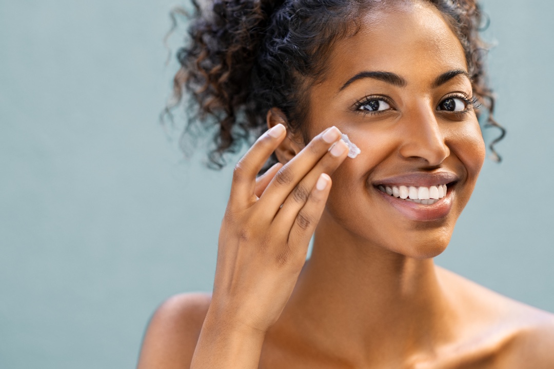 Girl with dark skin lightly rubs cream in to face