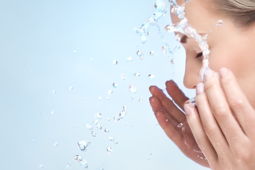 Caucasian woman with clear skin splashes face with water