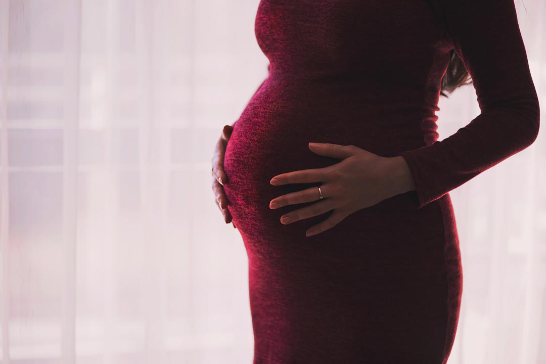 Pregnant woman holds hands on belly