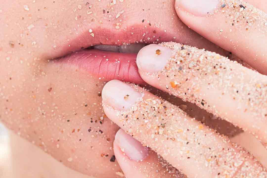 Close up of girls lips, whilst she touches her lips with grains of sand on her mouth and fingers